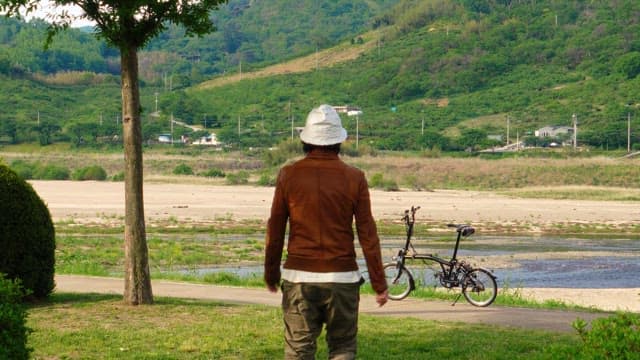 Man with a bicycle standing by a riverside path
