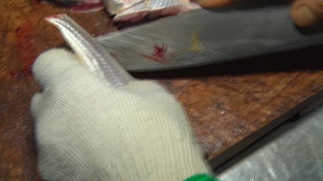 Sliced raw scaled sardine being prepared on a cutting board in a sushi restaurant kitchen