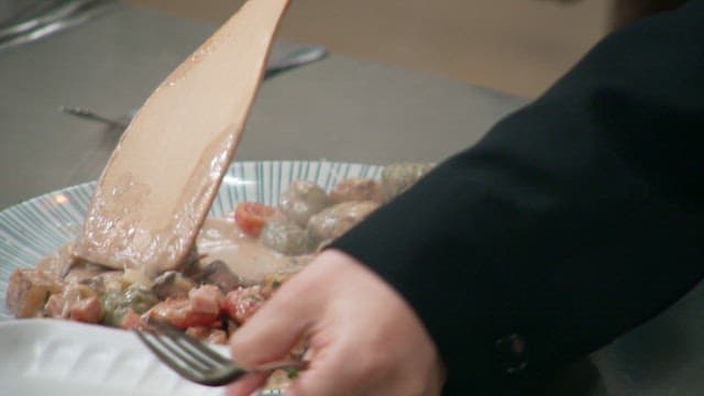 Serving a steaming creamy gnocchi on a plate with a wooden spatula