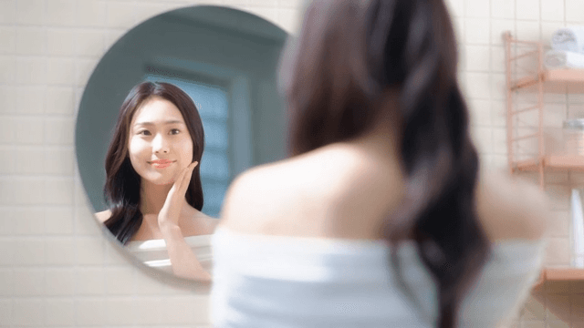 Woman smiling while touching her face in front of bathroom mirror