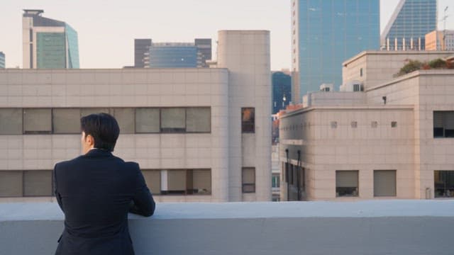 Man in a suit looking at buildings from a rooftop