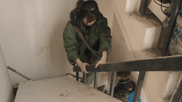 Two women climbing along a narrow and cluttered staircase indoors.