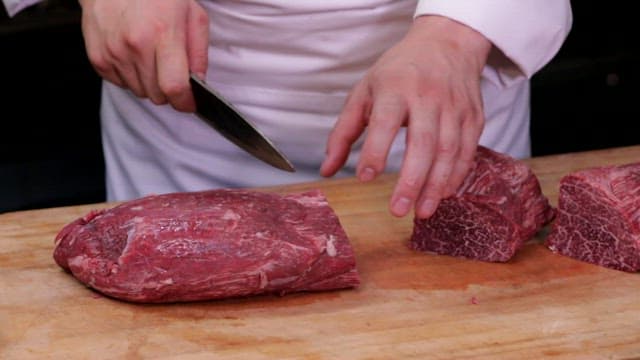 Chef slicing raw beef on a wooden board