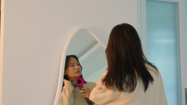 Woman drying her hair with dryer in front of a mirror