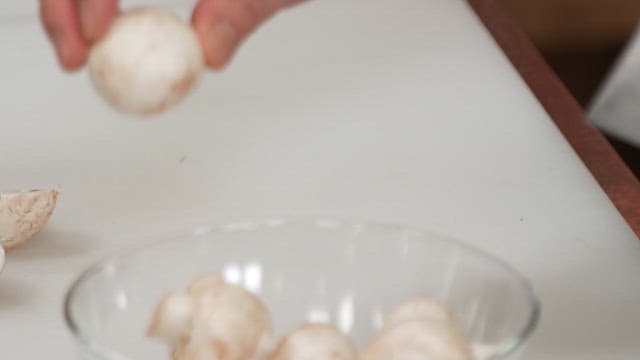 Cutting button mushrooms with a knife on a cutting board