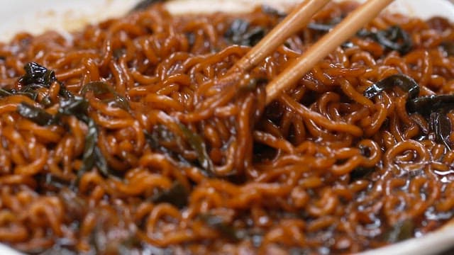 Chopsticks lifting saucy Jjajang Ramen in a bowl