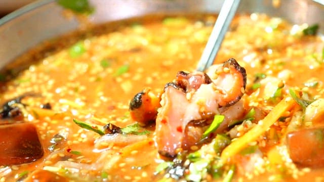 Picking up fresh top shell in cold raw fish soup using spoon