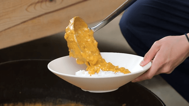 Person serving curry made of milk over rice