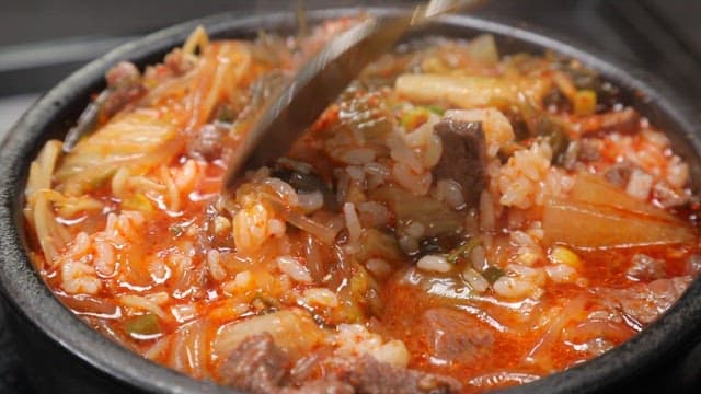 Spoonful of spicy Korean beef and rice soup in a clay pot