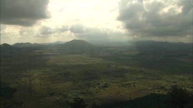 Sunlight shining through the cloudy sky over a plain with a view of the mountains