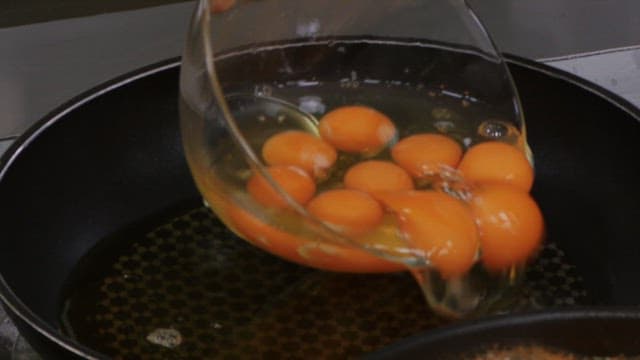 Pouring raw eggs into a hot frying pan