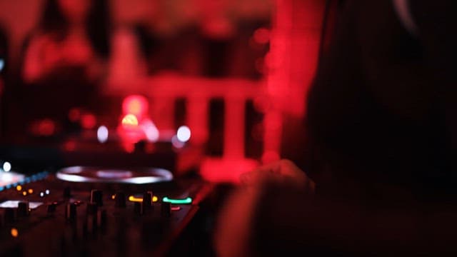 DJ Adjusting Mixer under Red Lights in Club