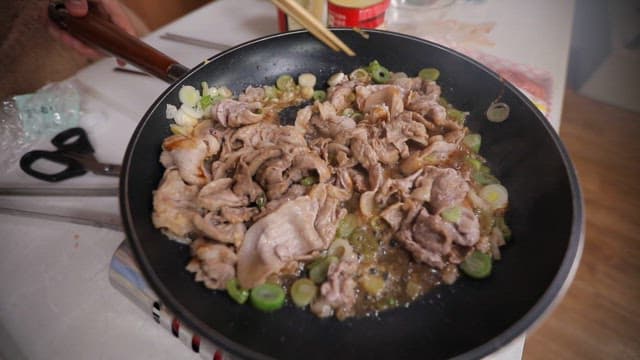 Cooking fresh meat with green onions in a black frying pan