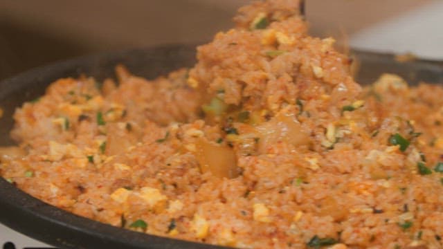 Cooking kimchi fried rice with egg in a hot pan on a stove with wooden spatula