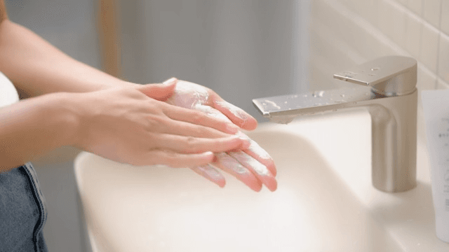 Person washing hands with soap at a sink in a clean bathroom