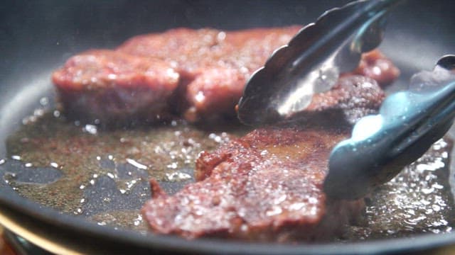 Beef steak being cooked in a frying pan