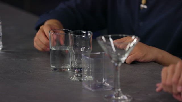 Pouring water from a glass into another glass on a table top