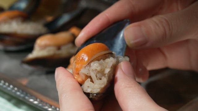 Hand preparing stuffed mussels in a detailed manner