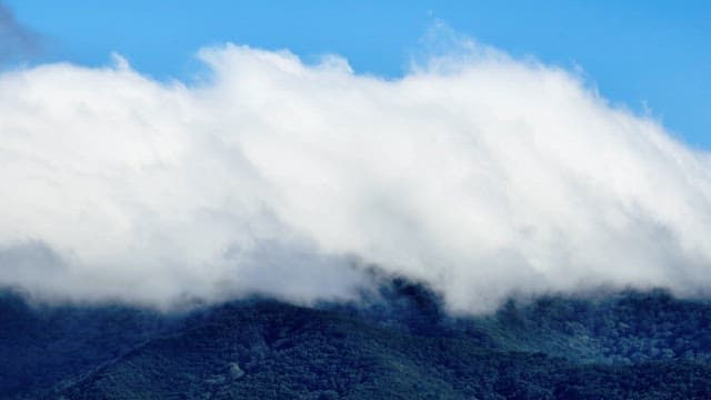 Clouds rolling over a lush green mountain
