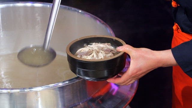 Pouring hot broth over bowl with rice and chicken