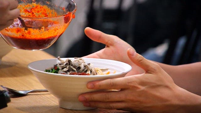Adding gochujang to a bowl of bibimbap topped with oyster mushrooms