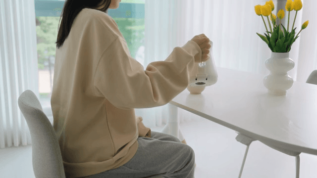 Woman pouring water into cup with coffee pot on table in bright living room
