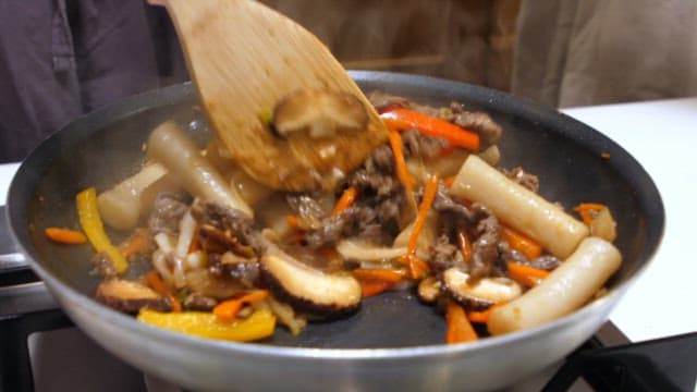 Making royal tteokbokki with meat and vegetables in a frying pan with a wooden spatula