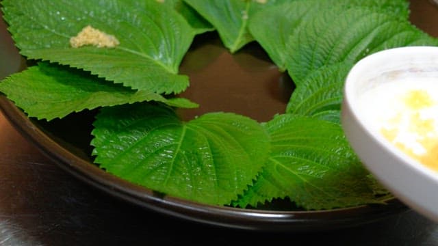 Hands plating flying fish roe on perilla leaves on a plate