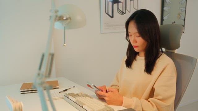 Woman using a smartphone at a desk in a calmly lit room
