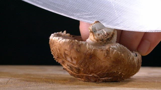 Slicing a mushroom on a wooden board with knife