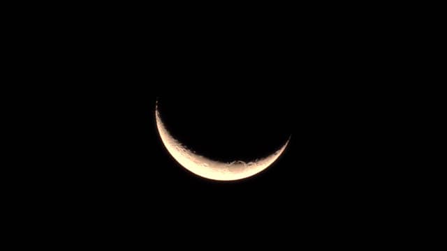 Crescent moon with craters visible in the dark night sky