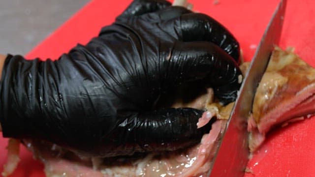 Slicing cooked ribs on a red cutting board with precision