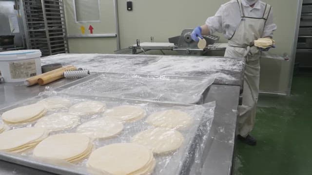 Worker placing batches of dough on a floured tray