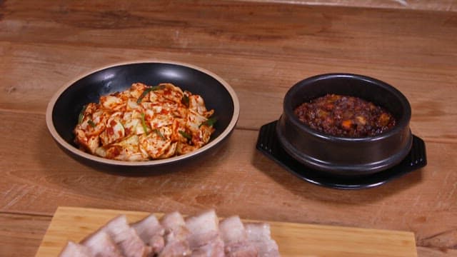A close-up view of Korean dishes including cabbage kimchi, boiled pork slices, and soybean paste ste