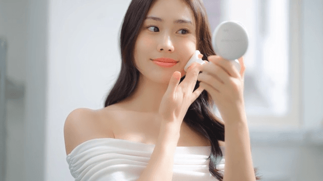 Woman in white top applying makeup with a mirror of cushion foundation