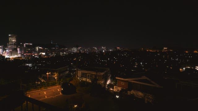 A nighttime urban cityscape with illuminated buildings and a neighborhood in the foreground