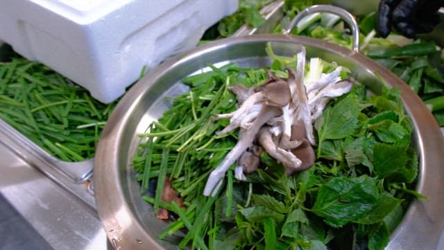 Fresh greens and mushrooms in a metal bowl on a kitchen countertop