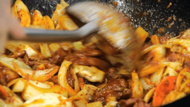 Spicy stir-fried octopus being cooked on wok in kitchen