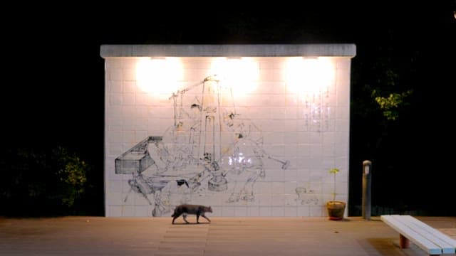 Cat walking past a mural at night