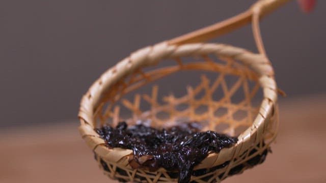 Filtering soaked seaweed in a transparent bowl using a wooden sieve