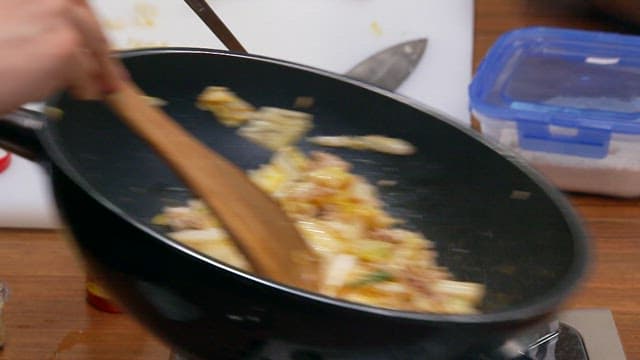 Stir-frying vegetables and meat in a frying pan on a stove