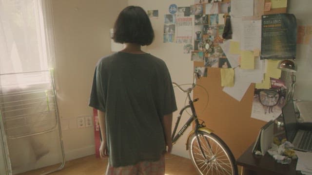 Woman exercising on a stationary bike near a cluttered desk in a sunlit room