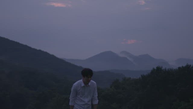 Back of a man smoking a cigarette on a mountain at sunset