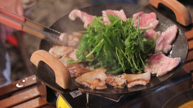 Water parsley and pork belly grilled on a hot iron plate outdoors