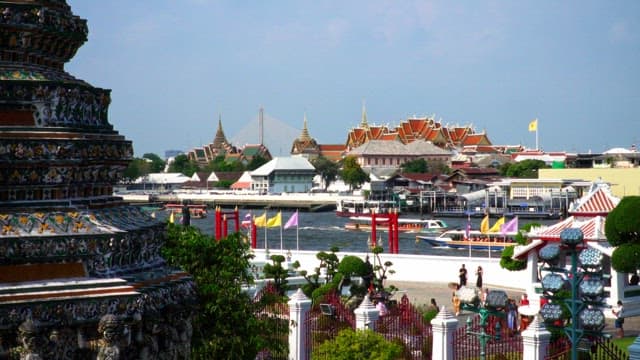 Tourists exploring a waterfront temple with passing boats on a sunny day