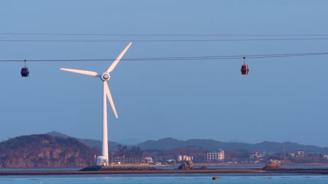 Coastal landscape with wind turbines and cable car lines against a peaceful sky during twilight