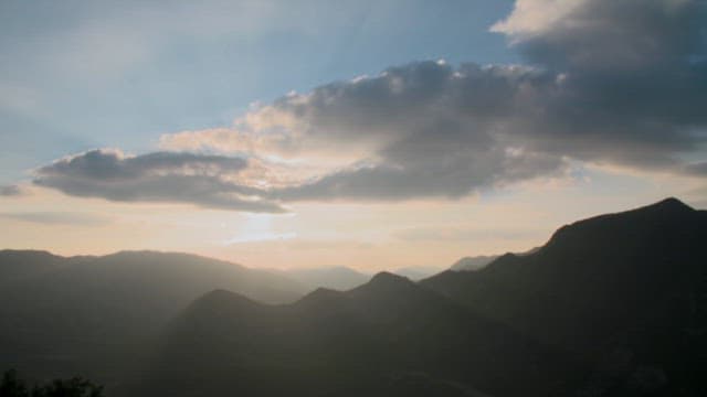 Sunset coloring the sky with clouds drifting over the mountain