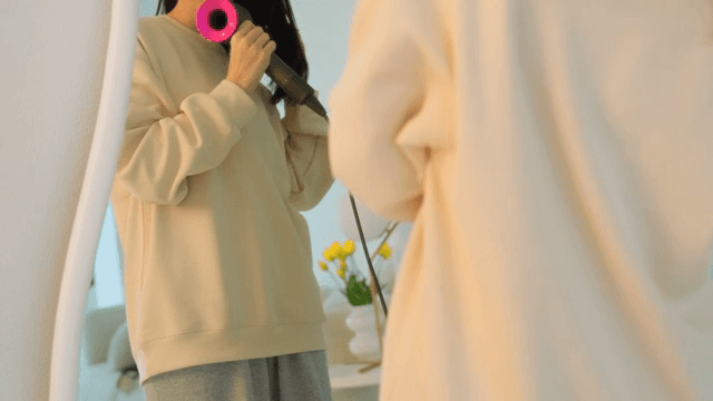 Woman drying her hair with dryer in front of a mirror