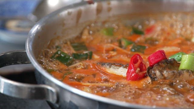 Close-up of a simmering pot of spicy stew with vegetables and abalone