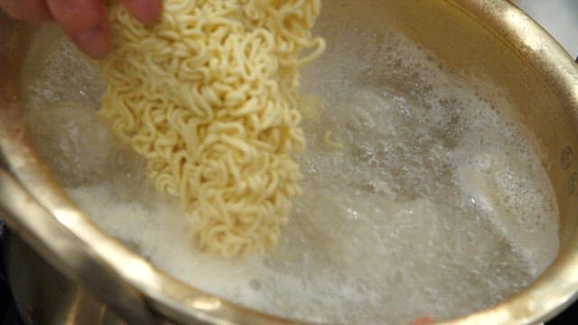 Instant noodles being added to boiling water